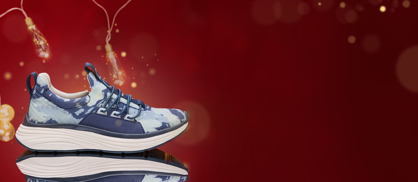 Zapatilla sin cordones Theora azul para mujer en Tie Dye, sobre un fondo rojo con luces encendidas en el fondo, tomada en un espejo